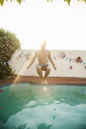 Shirtless man jumping into swimming pool against sky during sunset model released Symbolfoto property released AJOF00299