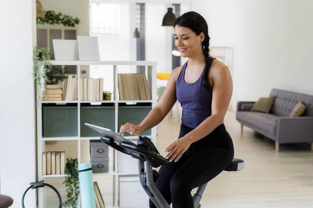 Young woman using digital tablet while sitting on exercise bike at home model released Symbolfoto property released GIOF09191