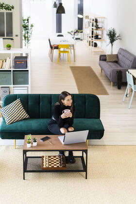 Young woman holding coffee cup while looking away in living room at home model released Symbolfoto property released GIOF09414