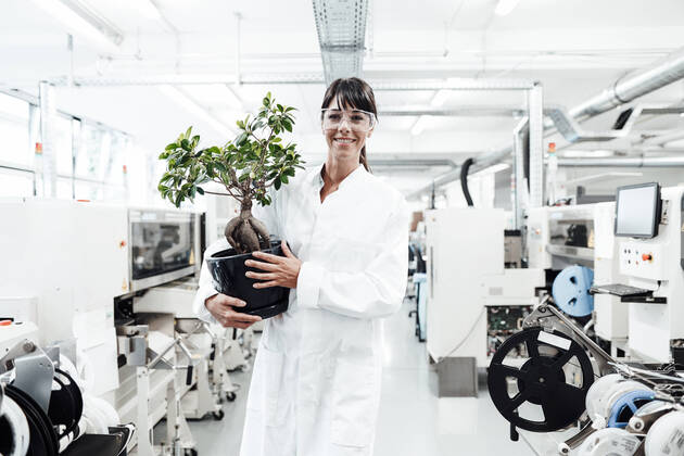 IMAGO Creative: Klimawandel - Zukunft und Innovation Smiling female scientist holding potted plant while standing amidst machineries at laboratory model released Symbolfoto property released JOSEF02177