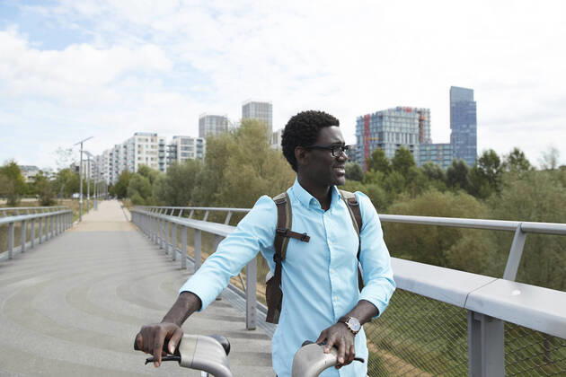 IMAGO Creative: Klimawandel - Zukunft und Innovation Smiling man looking away while walking with bicycle against sky in city model released Symbolfoto PMF01519