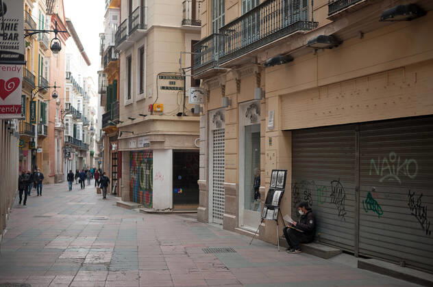 February 3, 2021, Malaga, Spain: A street painter wearing a face mask as a precaution against the spread of covid-19 seen sitting in front of a closed store as people walk along an empty and deserted Nueva street amid the partial lockdown caused by coronavirus pandemic. Malaga Spain - ZUMAs197 20210203_zab_s197_007 Copyright: xJesusxMeridax