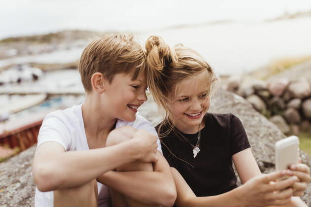 Smiling brother and sister taking selfie on smart phone at marina Sweden, Gothenburg, model released Copyright: xMaskotx , MA83891