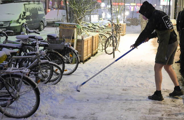 DEUTSCHLAND, Hamburg, Winter, Ladenangestellter in kurzer Hose befreit öffentliche Wege vom Schnee Hamburg Germany