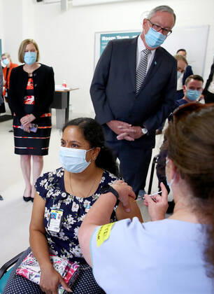 NSW COVID19 VACCINE ROLLOUT, Gayathry Vellangalloor Srinivasan, an Environmental Services Supervisor, is watched by NSW Chief Medical Health Officer Kerry Chant (left) and NSW Health Minister Brad Hazzard (right) as she receives the states first Pfizer vaccination at the Royal Prince Alfred Hospital Vaccination Hub in Sydney, Monday, February 22, 2021. Australia will begin its roll out of the Pfizer coronavirus vaccine on Monday, the country s most complicated logistical exercise to date. ( NO ARCHIVING, EDITORIAL USE ONLY, NO USE IN BOOKS WITHOUT CONSENT SYDNEY NSW AUSTRALIA  Copyright: xTobyxZernax 20210222001522236325