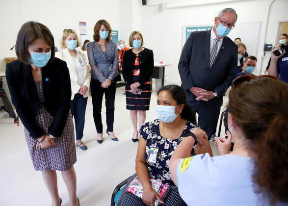 NSW COVID19 VACCINE ROLLOUT, Gayathry Vellangalloor Srinivasan, an Environmental Services Supervisor, is watched by NSW Premier Gladys Berejiklian (left), NSW Chief Medical Health Officer Kerry Chant (second right) and NSW Health Minister Brad Hazzard (right) as she receives the states first Pfizer vaccination at the Royal Prince Alfred Hospital Vaccination Hub in Sydney, Monday, February 22, 2021. Australia will begin its roll out of the Pfizer coronavirus vaccine on Monday, the country s most complicated logistical exercise to date. ( NO ARCHIVING, EDITORIAL USE ONLY, NO USE IN BOOKS WITHOUT CONSENT SYDNEY NSW AUSTRALIA  Copyright: xTobyxZernax 20210222001522236356