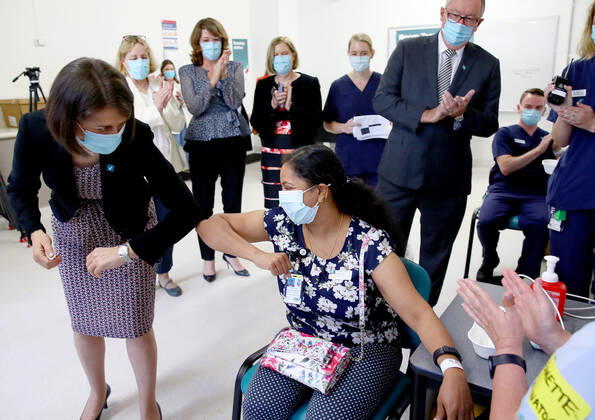 NSW COVID19 VACCINE ROLLOUT, Gayathry Vellangalloor Srinivasan, an Environmental Services Supervisor, is watched by NSW Premier Gladys Berejiklian (left), NSW Chief Medical Health Officer Kerry Chant (fourth right) and NSW Health Minister Brad Hazzard (second right) as she receives the states first Pfizer vaccination at the Royal Prince Alfred Hospital Vaccination Hub in Sydney, Monday, February 22, 2021. Australia will begin its roll out of the Pfizer coronavirus vaccine on Monday, the country s most complicated logistical exercise to date. ( NO ARCHIVING, EDITORIAL USE ONLY, NO USE IN BOOKS WITHOUT CONSENT SYDNEY NSW AUSTRALIA  Copyright: xTobyxZernax 20210222001522236514