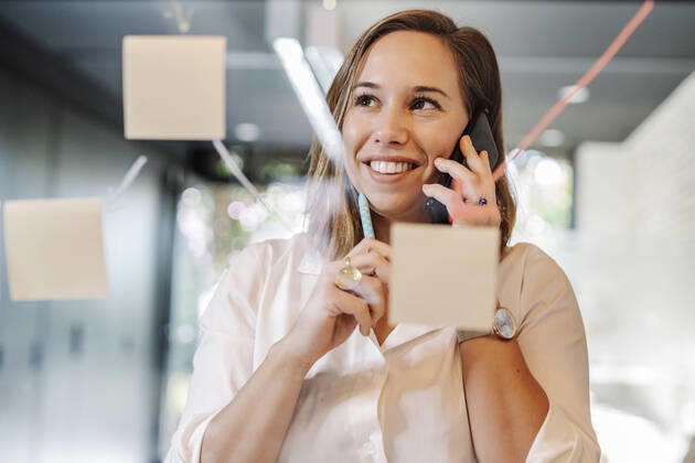 Close-up of smiling businesswoman talking over smart phone in office seen through glass wall model released Symbolfoto property released JCZF00457