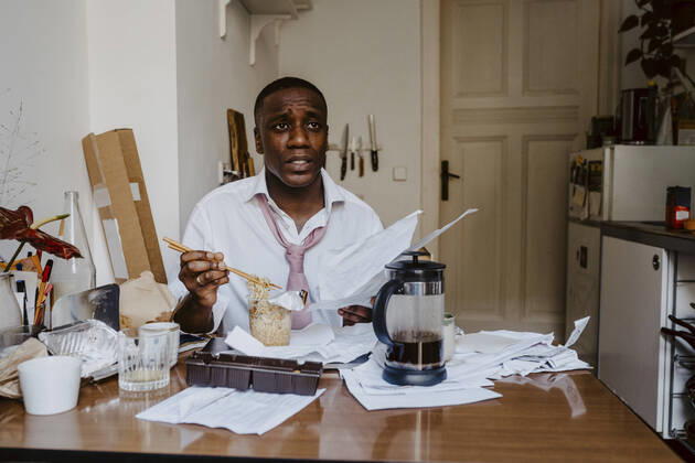 Thoughtful male entrepreneur with paper document having noodles at table in living room Germany, Berlin, model released, property released Copyright: xMaskotx , MA84917