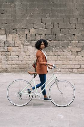 Side view of black woman in smart casual style walking along street with bike and looking at camera Copyright: xEduxFigueresx Model Released
