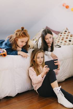 Cute little girls playing games on tablet and resting on soft bed while spending weekend together Copyright: xLightsyx Model Released
