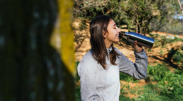 Side view of crop female hiker standing in forest and enjoying fresh water from metal bottle during hiking, Model released Copyright: xDavidxMunozx MR