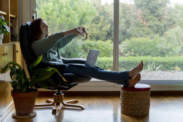 Mid adult woman stretching hand while sitting on chair at home model released Symbolfoto property released AFVF08326