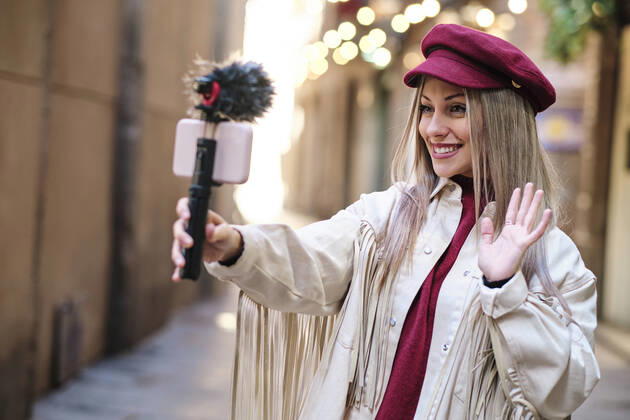 Smiling female vlogger waving hand while filming through mobile phone in city model released Symbolfoto AGOF00080