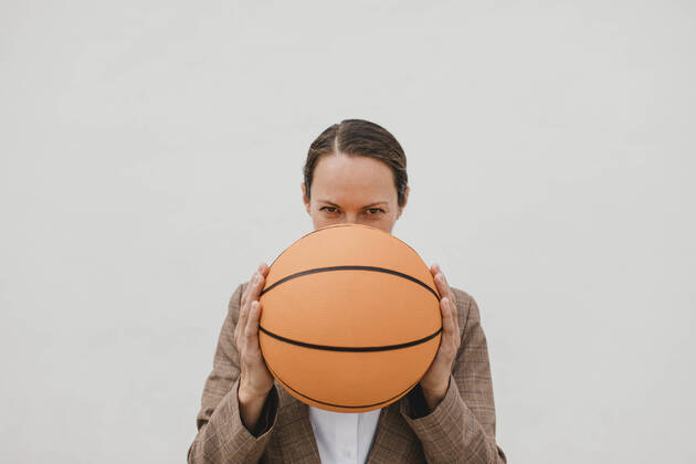 Businesswoman holding basketball in front of face against white wall during break model released Symbolfoto DMGF00515