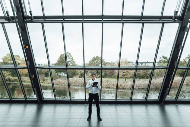 Male entrepreneur using digital tablet while using digital tablet against glass in office corridor model released Symbolfoto property released GUSF05407