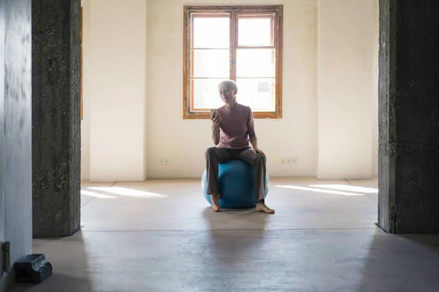 Businesswoman using smart phone while sitting on fitness ball in loft apartment model released Symbolfoto property released MOEF03638