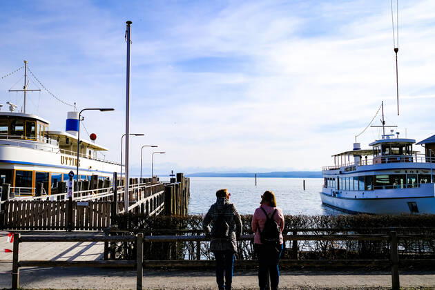 Spring weather at the Ammersee 25 03 2021 Excursionists in front of ships during spring weather in the harbour of Stegen Inning at the Ammersee Upper Bavaria with view towards the Alps Inning Bavaria Germany