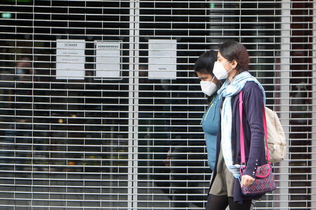 Women wearing masks walk past a shop closed with a rolling gate during the lockdown in the shopping street pedestrian zone Planken in downtown Mannheim, Baden Württemberg, Germany
