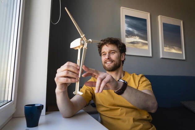 IMAGO Creative: Corporate: Klimaschutz, Digitalisierung und Urbanisierung IMAGO Creative: Klimawandel - Zukunft und Innovation Smiling businessman holding wind turbine model while sitting at home model released Symbolfoto property released VPIF03875