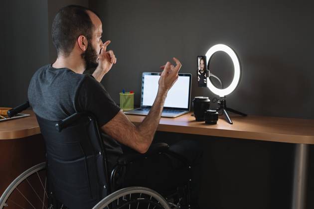 Vlogger filming through mobile phone with circular strobe tripod while sitting on wheelchair at studio model released Symbolfoto property released XLGF01348