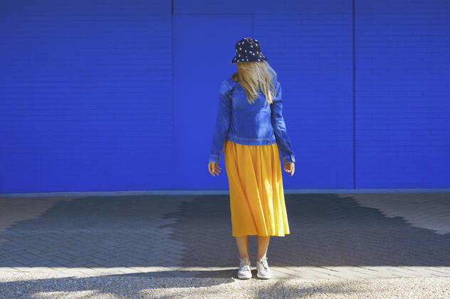 Blond woman wearing bucket hat standing in front of blue wall model released Symbolfoto AZF00278