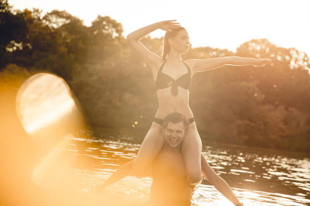 Young woman sitting on shoulders of young man standing in lake, enjoying the sun model released Symbolfoto GUSF02346