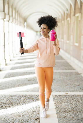 Smiling woman vlogging with smart phone while walking in arcade model released Symbolfoto JCCMF01778