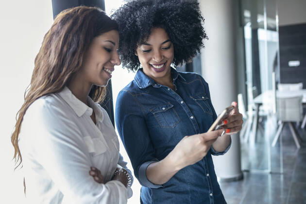 Smiling female entrepreneurs discussing over mobile phone at office model released Symbolfoto property released JSRF01501