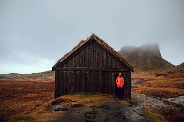 IMAGO Creative: Klimawandel - Nachhaltiges Reisen Young tourist standing near hut between wild lands near high stone hills and cloudy sky, Model released Copyright: xAdrianxSavax MR