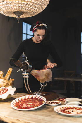 Female owner cutting meat on ham holder at restaurant model released Symbolfoto property released JAQF00556