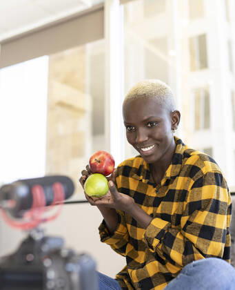 Short haired woman holding apple while vlogging at home model released Symbolfoto property released JCCMF02323