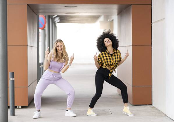 Female friends making obscence gesture while dancing at parking lot model released Symbolfoto JCCMF02353