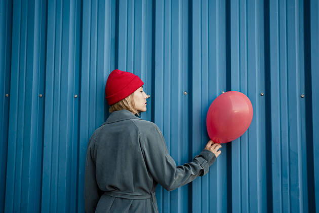 Mid adult woman holding red balloon by blue shutter model released Symbolfoto RCPF00986