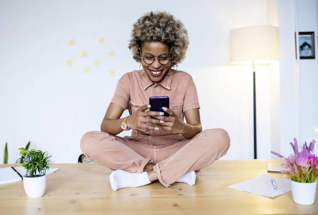 Female professional using smart phone while sitting cross-legged on desk at home office model released Symbolfoto property released RFTF00067