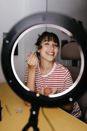 Smiling female influencer applying make-up while vlogging at studio model released Symbolfoto property released TCEF01763