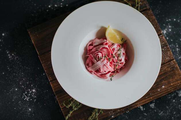Top view of appetizing vegan pink beetroot pasta with lemon slice and thyme sprig served on wooden board on black table Copyright: xCamillexGirardx Model Released