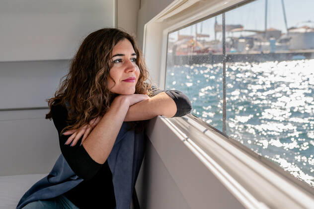 Tranquil female sitting in cabin of catamaran and looking out of window while admiring amazing view of sea on sunny day, Model released, Property released Copyright: xCarlosxPintaux MR