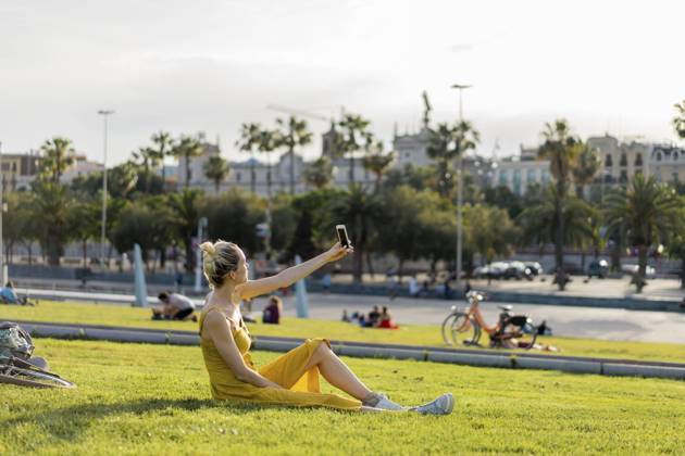 IMAGO Creative: Sommer, Sommertage im Stadtpark Young woman taking selfie through smart phone while sitting at park model released Symbolfoto AFVF08865