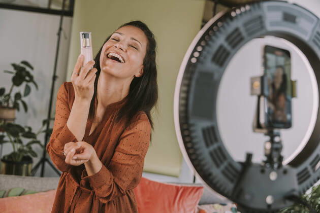 Laughing female influencer holding foundation while vlogging at home model released Symbolfoto property released MFF08081