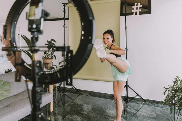 Female fitness trainer showing kicks near backdrop while vlogging at home model released Symbolfoto property released MFF08095