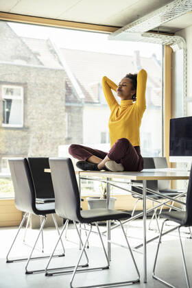 Businesswoman with arms raised meditating on desk at office model released Symbolfoto property released UUF23346