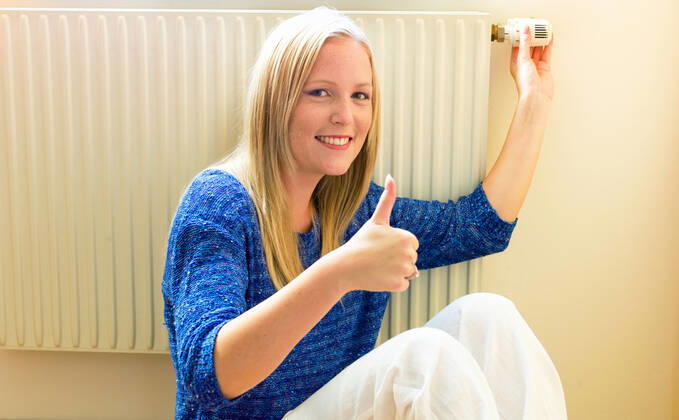 A young woman sits in front of a radiator in winter Room temperature is too low McPBBO McPBBO