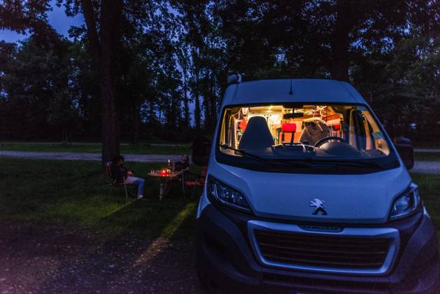 Campers sitting on camping chairs in front of their camper at blue hour on a warm summer evening Baden Württemberg, Germany On the road with a campervan