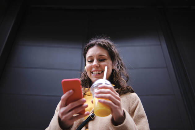 Smiling young woman with smoothie using smart phone near black door model released Symbolfoto ASGF00635