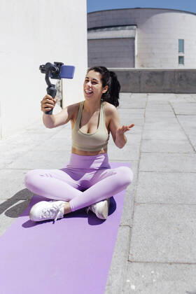 Smiling female athlete vlogging through smart phone while sitting on exercise mat during sunny day model released Symbolfoto EGHF00026