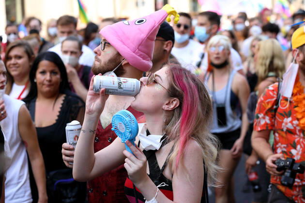 Berliner CHRISTOPHER STREET DAY 2021 - CSD - Am 24. Juli 2021 zieht der CSD in Berlin unter dem Motto SAVE OUR COMMUNITY SAVE YOUR PRIDE zum 43. Mal durch die Hauptstadt. Bunte Demoteilnehmer teils mit Mundschutzmasken im Protestzug. Vorne im Bild: Junge Frau mit einem Getränk kühlt sich mit einem Mini-Ventilator. Die bunte CSD-Parade startete in diesem Jahr als Demonstration an der Leipziger Straße, führte über den Potsdamer Platz, vorbei am Denkmal für die im Nationalsozialismus verfolgten Homosexuellen zum Brandenburger Tor und über die Siegessäule zur Urania. Aufgrund der Corona-Pandemie fand die Demonstration ausschließlich unter Einhaltung der vom Berliner Senat erlassenen Vorgaben statt. Die in den Vorjahren übliche Ab