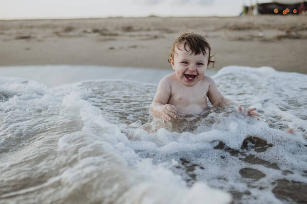 Male toddler laughing while sitting in water at beach during sunset model released Symbolfoto GMLF00754