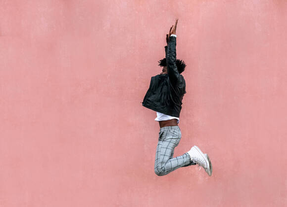 Creative Highlights Symbolbilder Mid adult man with arms raised jumping by pink wall in city model released Symbolfoto MGOF04458