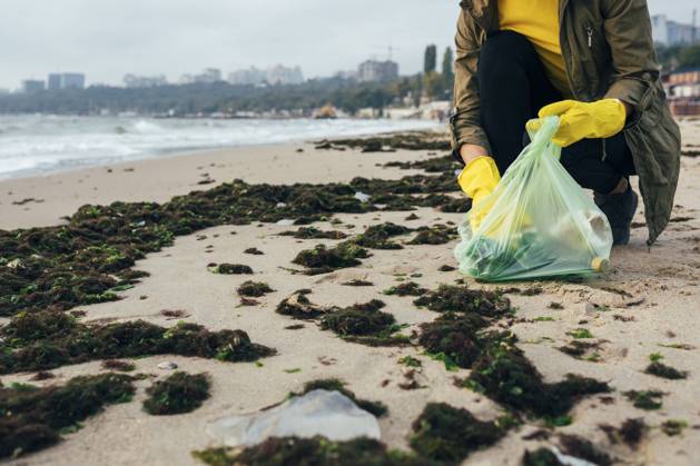 IMAGO Nature: Unsere Erde, Umweltverträgliche Herausforderungen, Plastikmüll Environmentalist collecting garbage in garbage bag while crouching at beach model released Symbolfoto OYF00247
